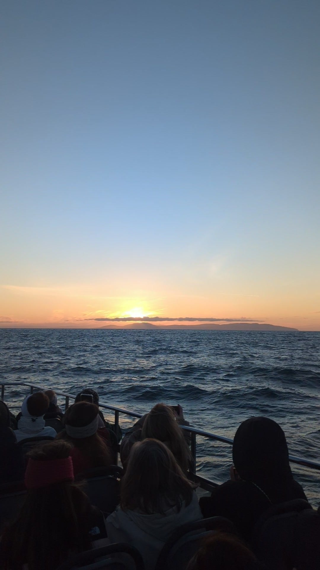 Guests seen from behind on the deck of Selkie, watching the sun rise over the sea on the Darkness Into Light sunrise sailing from Ballycastle in May 2026.