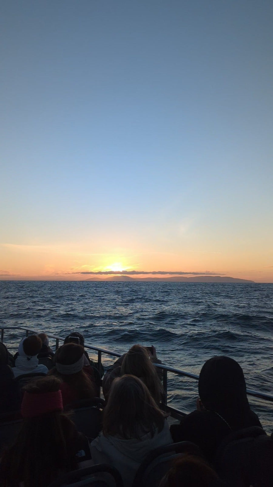 Guests seen from behind on the deck of Selkie, watching the sun rise over the sea on the Darkness Into Light sunrise sailing from Ballycastle in May 2026.