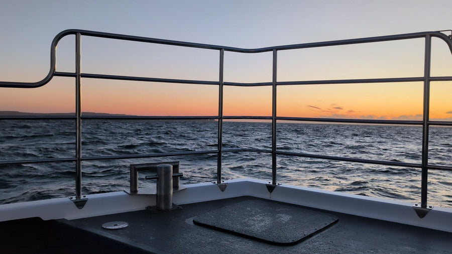 The bow rail of the boat Selkie in the foreground with an orange band of dawn light on the horizon, on a sunrise sailing from Ballycastle.